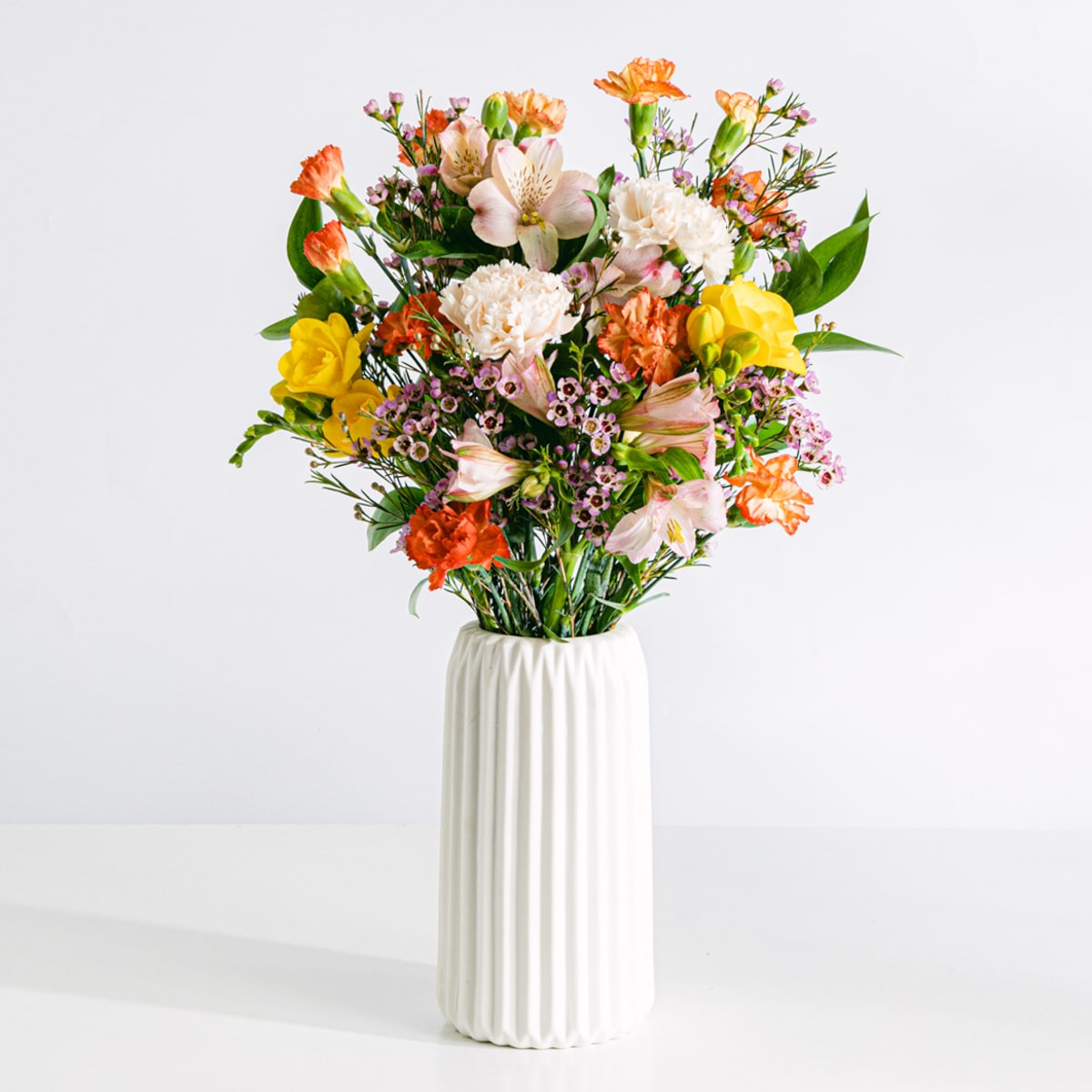 Bouquet de flores de cera cor-de-rosa, alstroemérias cor-de-rosa, frésias amarelas e cravos cor de laranja em miniatura com jarra