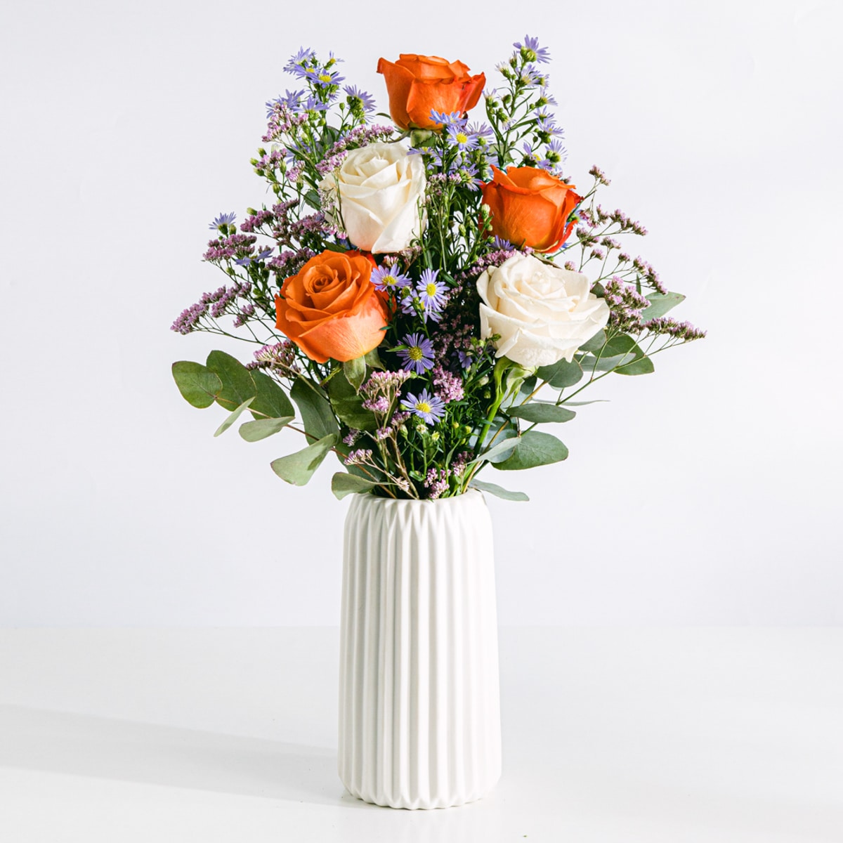 Buquê de flores incluindo rosas brancas, laranja e áster com vaso
