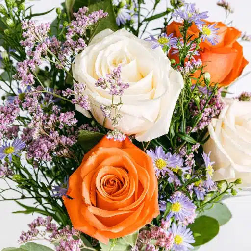 Detalle de ramo de flores que incluye rosas blancas, naranjas y aster