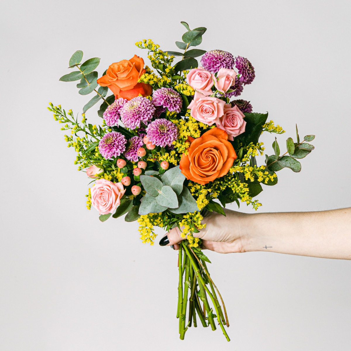 Mão segurando um ramo de rosas cor de laranja e rosas ramificadas