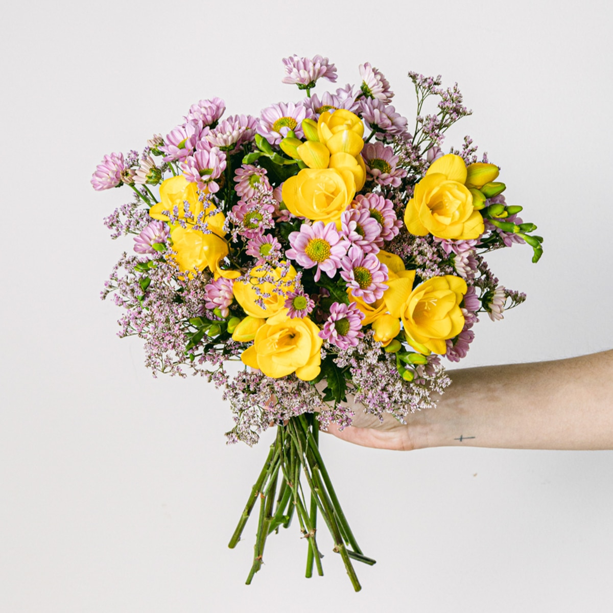 Hand mit Strauß aus gelben Freesien und rosa Limonium