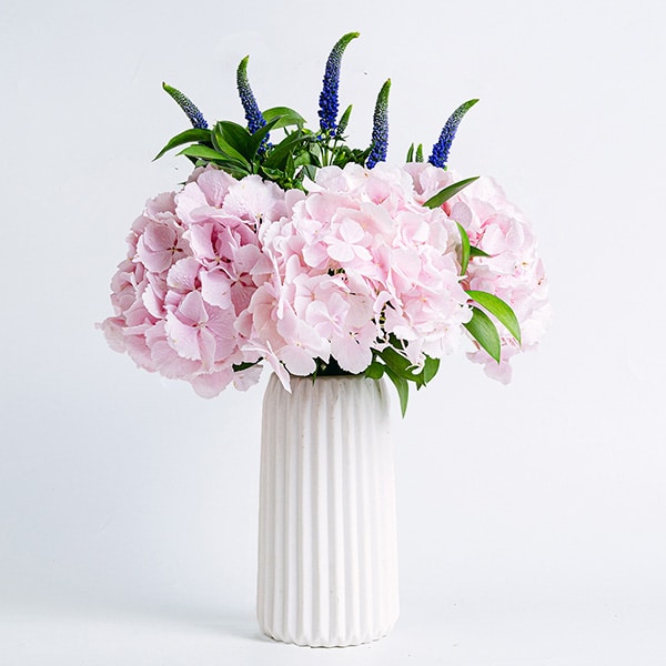Bouquet di orchidee e veroniche rosa in un vaso bianco con una candela come decorazione