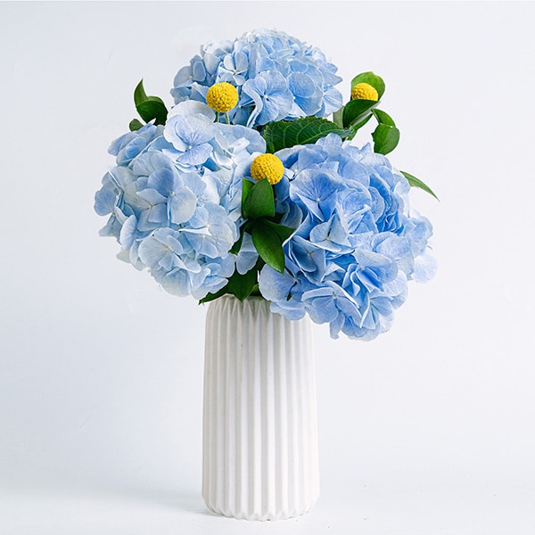 Hortensias azules en un jarrón blanco con una vela como decoración